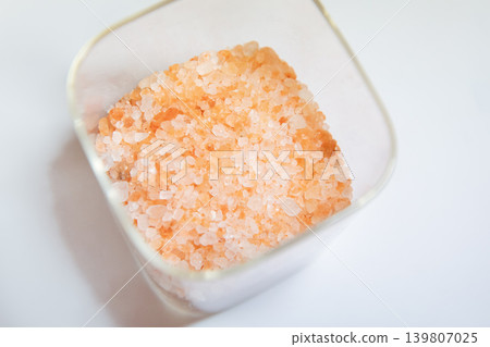 Pink Himalayan salt in a glass container. Mineral seasoning for cooking and health. Natural ingredient for spa and organic wellness lifestyle. Food background with coarse raw crystal. Pink Himalayan salt in a glass container. Mineral seasoning for cooking and health. Natural ingredient for spa and organic wellness lifestyle. Food background with coarse raw crystal. 139807025