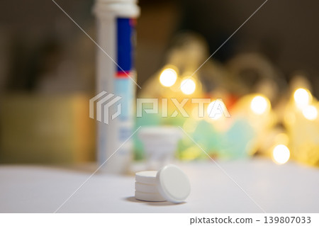 Effervescent tablet on table with tube in blurred background. Medical pill for health treatment and vitamin supplement. Nutritional care and pharmacy product for wellness daily routine. Effervescent tablet on table with tube in blurred background. Medical pill for health treatment and vitamin supplement. Nutritional care and pharmacy product for wellness daily routine. 139807033