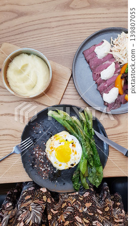 Woman eating delicious meal with roasted beef, fried egg, lettuce and mashed potato at restaurant. Gourmet dinner set served on plate. Top view of healthy food culture and dining. Woman eating delicious meal with roasted beef, fried egg, lettuce and mashed potato at restaurant. Gourmet dinner set served on plate. Top view of healthy food culture and dining. 139807055