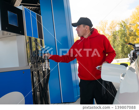 Man refueling his car at the gas station. Driver holding fuel nozzle to pour gasoline into vehicle tank. Automotive service and energy consumption fuel industry concept for road travel. Man refueling his car at the gas station. Driver holding fuel nozzle to pour gasoline into vehicle tank. Automotive service and energy consumption fuel industry concept for road travel. 139807088