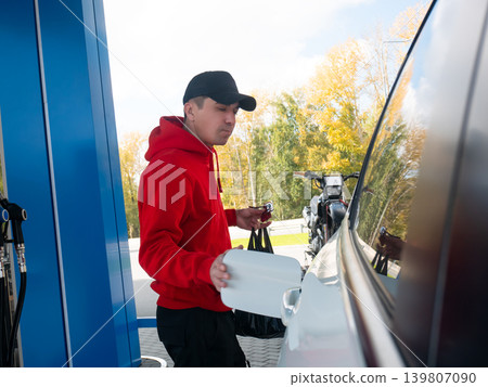 Man opening fuel tank door of his car at gas station. Driver refueling vehicle, holding plastic bag at service station. Transportation, travel, daily routine and road trip concept. 139807090