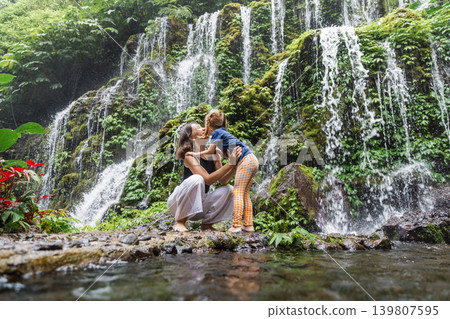 Happy mother and daughter hugging near waterfall in Bali 139807595