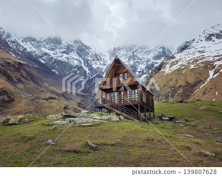 Snow-capped peaks loom above a rustic wooden cabin Snow-capped peaks loom above a rustic wooden cabin 139807628