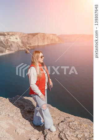 Woman cliff sea standing on a high rocky edge overlooking the blue ocean during a bright sunny day 139807648