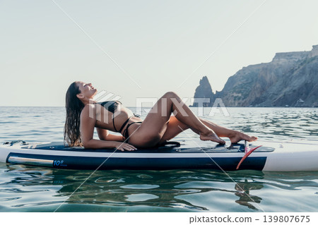 Woman Paddleboard Ocean - Relaxing on paddleboard in ocean, enjoying the sun and the view of the coastline. 139807675