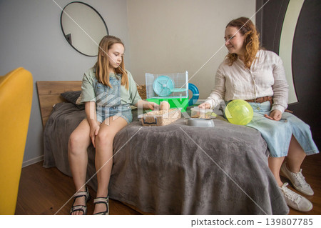Mom and girl sit on a bed in a small room with pet. Mom and girl sit on a bed in a small room with pet. 139807785