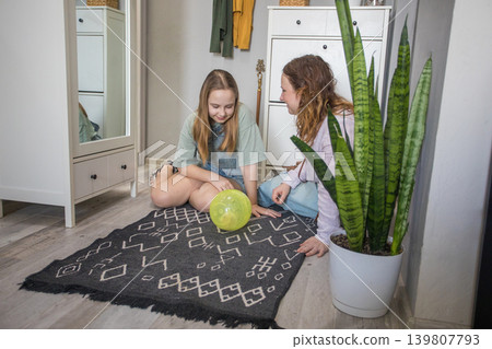 Mom and girl sit on the floor engaging with a green ball with pet hamster in a home living room. Mom and girl sit on the floor engaging with a green ball with pet hamster in a home living room. 139807793