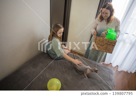 A girl sits on a bed looking at a woman who brings a basket filled with pet supplies. A girl sits on a bed looking at a woman who brings a basket filled with pet supplies. 139807795