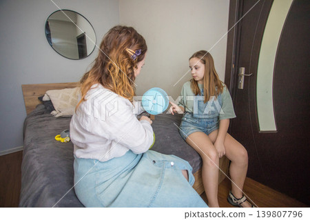 In a room with natural light, two girls work on putting together a pet. One girl holds a green ball In a room with natural light, two girls work on putting together a pet. One girl holds a green ball 139807796