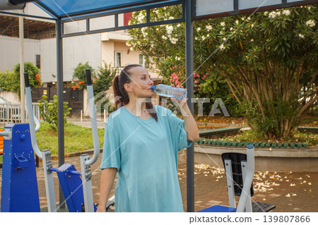Beautiful woman drinking water from a plastic bottle after a workout Beautiful woman drinking water from a plastic bottle after a workout 139807866