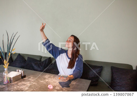 Cute woman waving her hand while sitting on table in cafe Cute woman waving her hand while sitting on table in cafe 139807867