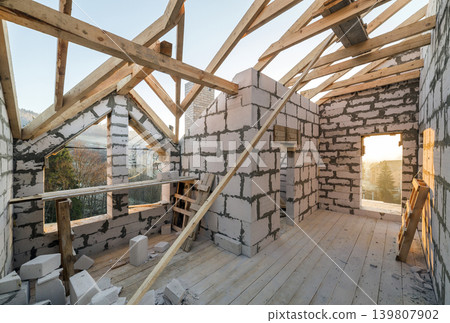 House interior under construction and renovation. Energy saving walls of hollow foam insulation blocks and bricks, ceiling beams and roof frame. 139807902