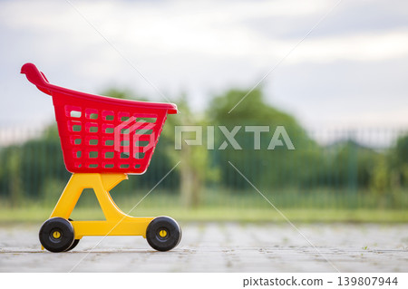 Bright plastic colorful shopping cart toy outdoors on sunny summer day. Bright plastic colorful shopping cart toy outdoors on sunny summer day. 139807944