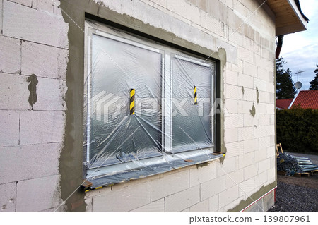 Window of a house under construction covered with protective plastic film. Window of a house under construction covered with protective plastic film. 139807961