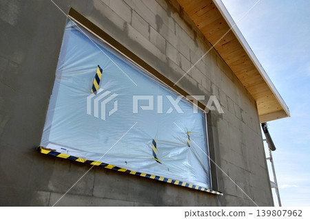 Window of a house under construction covered with protective plastic film. Window of a house under construction covered with protective plastic film. 139807962