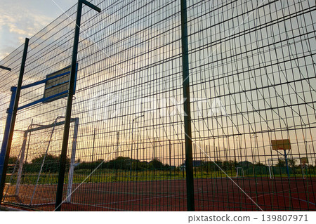 Outdoors mini football and basketball court with ball gate and basket surrounded with high protective fence. 139807971