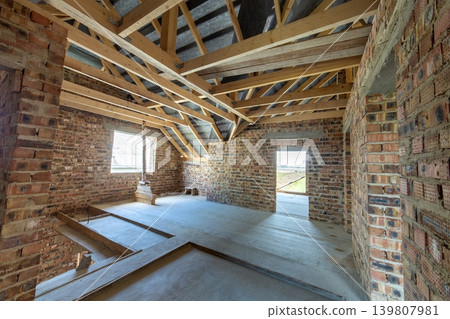 Attic of a building under construction with wooden beams of a roof structure and brick walls. Attic of a building under construction with wooden beams of a roof structure and brick walls. 139807981