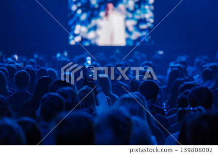 Audience recording live concert with smartphone in blue lit venue, crowd watching stage performance Audience recording live concert with smartphone in blue lit venue, crowd watching stage performance 139808002