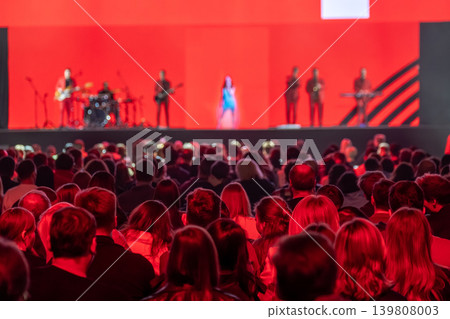 Live concert crowd watching band on stage with red lighting and singer 139808003