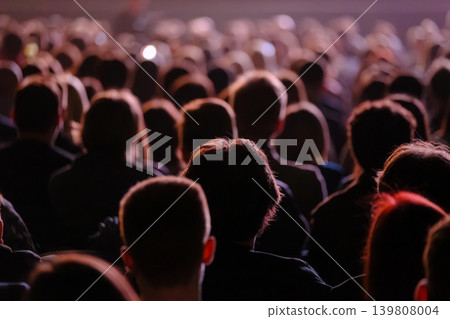 Audience in dimly lit venue watching performance, crowd silhouettes at indoor event Audience in dimly lit venue watching performance, crowd silhouettes at indoor event 139808004