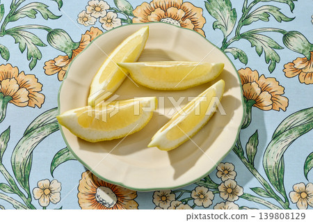 Sliced Lemon Wedges on a White Ceramic Plate on a Floral Tablecloth. Top View Sliced Lemon Wedges on a White Ceramic Plate on a Floral Tablecloth. Top View 139808129