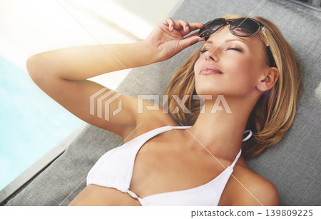 Woman, swimming pool and bikini or sunglasses in summer for holiday travel, rest or vacation. Female person, eyewear and patio furniture for sunbathing in sunshine for stress free, paradise or Miami Woman, swimming pool and bikini or sunglasses in summer for holiday travel, rest or vacation. Female person, eyewear and patio furniture for sunbathing in sunshine for stress free, paradise or Miami 139809225