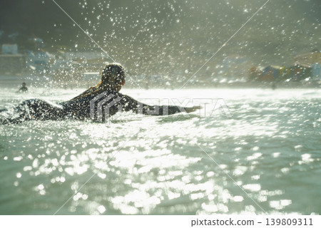 Swimming, splash and woman on surfboard in ocean for fitness, exercise or recreation in summer. Sports, travel or training with surfer person in sea for vacation, holiday or leisure hobby from back Swimming, splash and woman on surfboard in ocean for fitness, exercise or recreation in summer. Sports, travel or training with surfer person in sea for vacation, holiday or leisure hobby from back 139809311