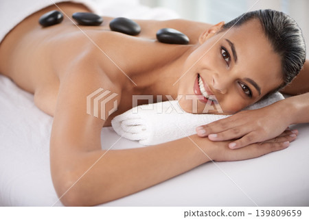 Relax, hot stone and portrait of woman with massage at spa for wellness, health and back treatment. Self care, smile and young female person with cosmetic warm stone back therapy at beauty salon. Relax, hot stone and portrait of woman with massage at spa for wellness, health and back treatment. Self care, smile and young female person with cosmetic warm stone back therapy at beauty salon. 139809659