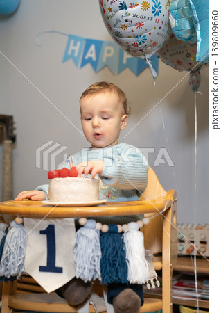 Toddler Baby boy eating berries from his birthday cake. First birthday family celebration. Child celebrates birthday with cake and decorations at home with balloons and decoration. Vertical card. Toddler Baby boy eating berries from his birthday cake. First birthday family celebration. Child celebrates birthday with cake and decorations at home with balloons and decoration. Vertical card. 139809660