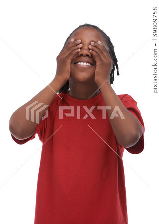 Child, boy and cover eyes with hands for secret or surprise, hiding or protection, red tshirt and smile on white background. Emoji, happy African kid not looking for announcement or news in studio 139809758