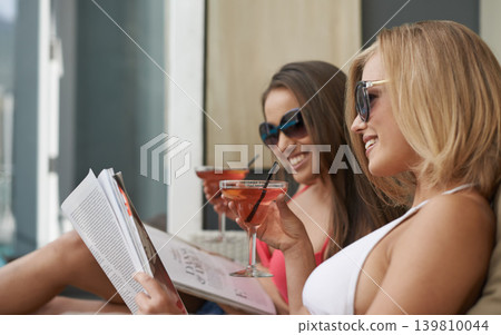 Friends, women and relaxing with cocktail at resort, bonding and drinking wine on tropical vacation. People, reading news and magazine for gossip on summer holiday, weekend trip and travel to retreat 139810044