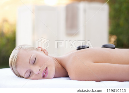 Spa, woman and hot stone on massage bed with peace for wellness, zen and beauty treatment for body care. Person, relax and stress relief at resort, salon table and luxury on holiday or vacation Spa, woman and hot stone on massage bed with peace for wellness, zen and beauty treatment for body care. Person, relax and stress relief at resort, salon table and luxury on holiday or vacation 139810213
