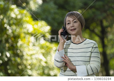 Senior women taking photos with their smartphones and chatting in a park surrounded by fresh greenery. 139810284