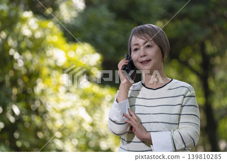 Senior women taking photos with their smartphones and chatting in a park surrounded by fresh greenery. 139810285