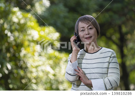 一群老年婦女在綠樹環繞的公園裡，用智慧型手機拍照、聊天。 139810286