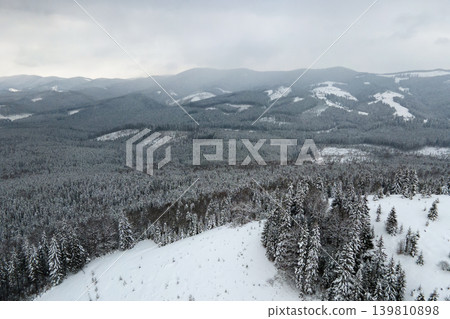 Aerial foggy landscape with evergreen pine trees covered with fresh fallen snow after heavy snowfall in winter mountain forest on cold quiet evening. Aerial foggy landscape with evergreen pine trees covered with fresh fallen snow after heavy snowfall in winter mountain forest on cold quiet evening. 139810898