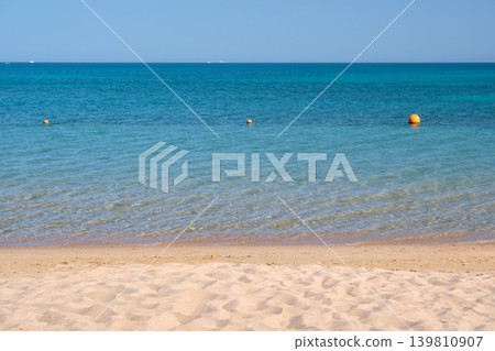 Seascape with surface of blue sea water with small ripple waves crashing on yellow sandy beach. Travel and vacations concept. Seascape with surface of blue sea water with small ripple waves crashing on yellow sandy beach. Travel and vacations concept. 139810907