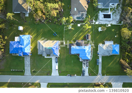 Aerial view of damaged in hurricane Ian houses roofs covered with blue protective tarp against rain water leaking until replacement of asphalt shingles Aerial view of damaged in hurricane Ian houses roofs covered with blue protective tarp against rain water leaking until replacement of asphalt shingles 139810920