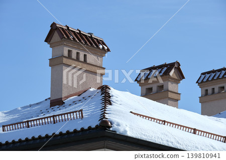 Closeup of house roof top covered with snow in cold winter. Tiled covering of building in wintertime weather Closeup of house roof top covered with snow in cold winter. Tiled covering of building in wintertime weather 139810941