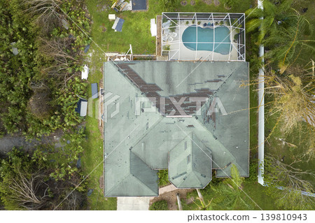 Damaged house roof with missing shingles after hurricane Ian in Florida. Consequences of natural disaster Damaged house roof with missing shingles after hurricane Ian in Florida. Consequences of natural disaster 139810943