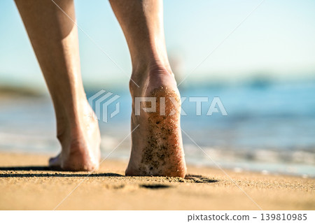 Close up of woman feet walking barefoot on sand leaving footprints on golden beach. Vacation, travel and freedom concept. People relaxing in summer. Close up of woman feet walking barefoot on sand leaving footprints on golden beach. Vacation, travel and freedom concept. People relaxing in summer. 139810985
