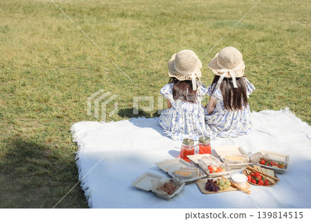 一張姊妹倆在夏日公園野餐的照片,照片中可以看到她們的背影和食物。 一張姊妹倆在夏日公園野餐的照片,照片中可以看到她們的背影和食物。 139814515
