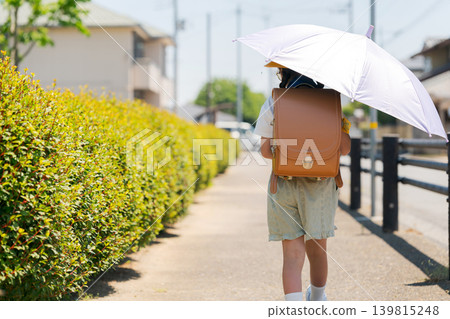 The back view of an elementary school student walking to school with a parasol. The back view of an elementary school student walking to school with a parasol. 139815248