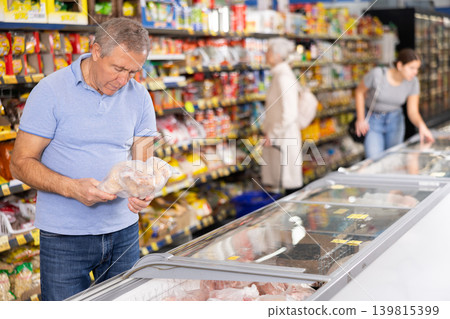 Man purchaser choosing frozen chicken in supermarket Man purchaser choosing frozen chicken in supermarket 139815399