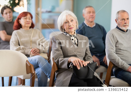 Interested group of people of different ages sitting on chairs and listening lecture in conference hall Interested group of people of different ages sitting on chairs and listening lecture in conference hall 139815412