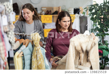 During November sales, Latin woman choose fur coat, other client in background During November sales, Latin woman choose fur coat, other client in background 139815519