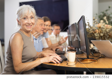 Portrait of an elderly positive woman working on computer with group of friends while attending PC classes in nursing home Portrait of an elderly positive woman working on computer with group of friends while attending PC classes in nursing home 139815532