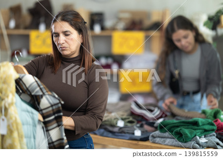 During November sales, Latin woman choose checkered coat-jacket, other client in background During November sales, Latin woman choose checkered coat-jacket, other client in background 139815559