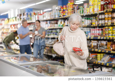 Elderly woman buyer carefully chooses frozen food in grocery store freezer 139815561