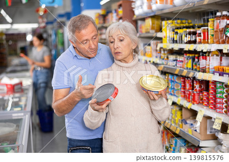 Elderly couple choosing canned food in tin cans in grocery store Elderly couple choosing canned food in tin cans in grocery store 139815576
